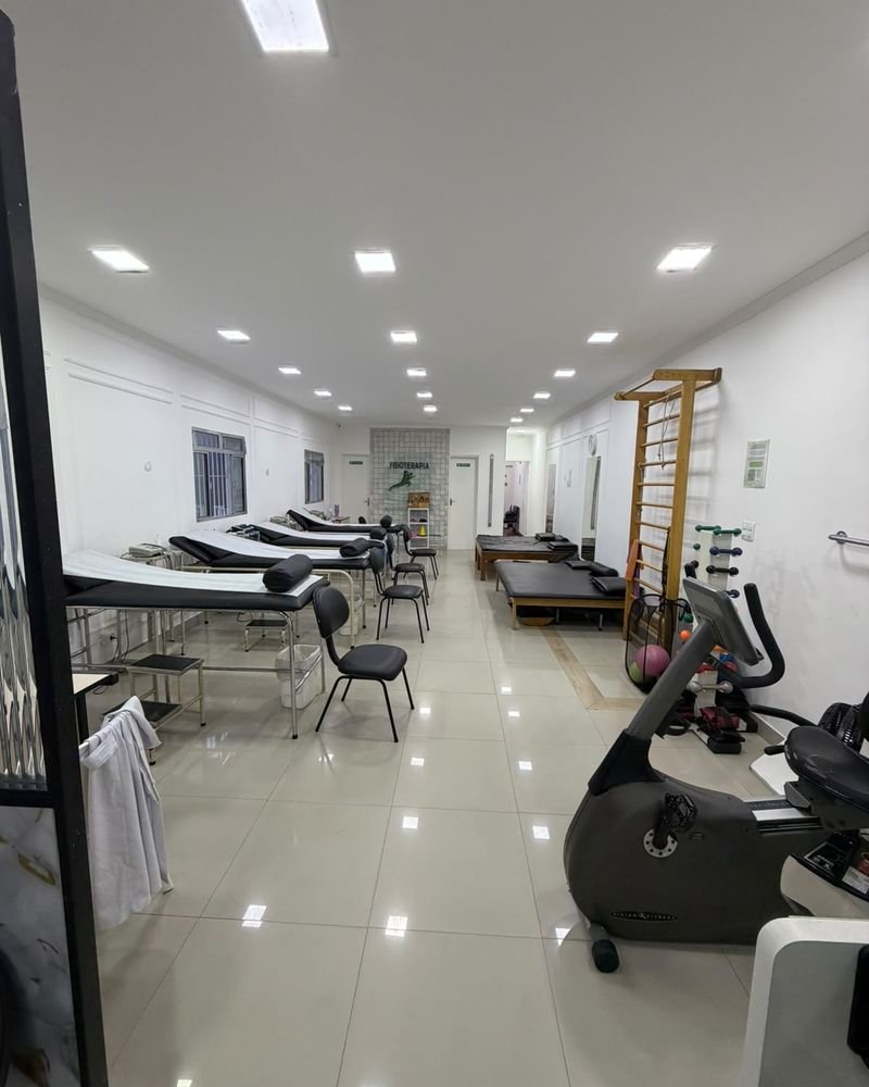 Salão de fisioterapia amplo e iluminado, com macas, espaldar e bicicleta ergométrica